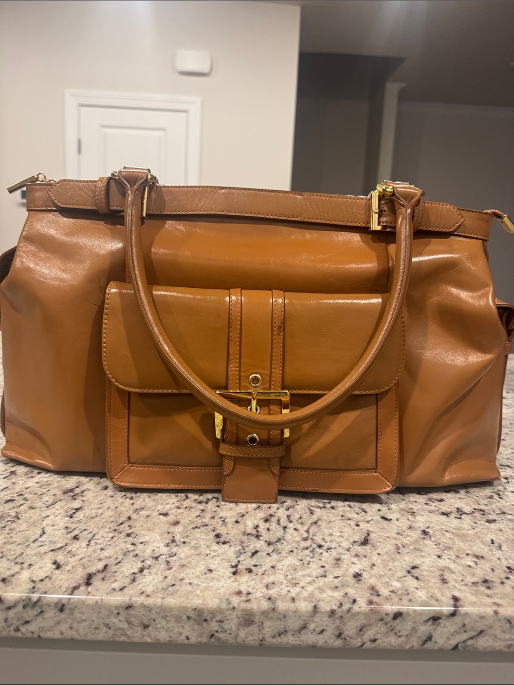 The Find Classic Tan Leather Weekender Travel Bag with Gold Hardware Buckle.